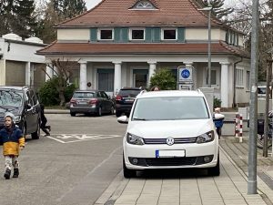 Ein PKW steht auf dem Bürgersteig, ein Kind läuft auf der Fahrbahn